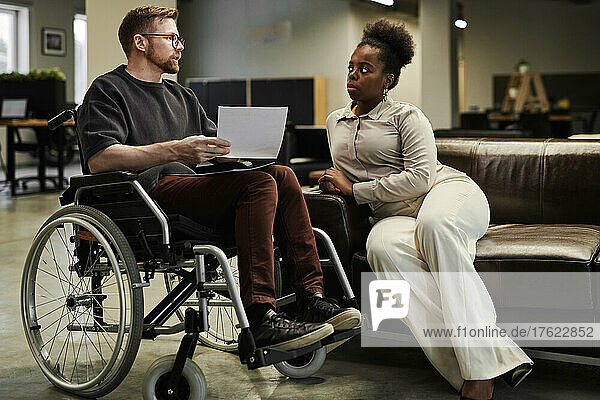 Geschäftsfrau hört im Büro einem behinderten Kollegen im Rollstuhl zu