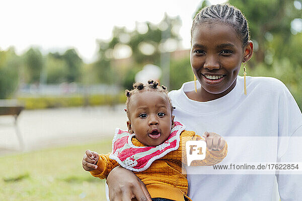 Smiling young woman with cute daughter at park
