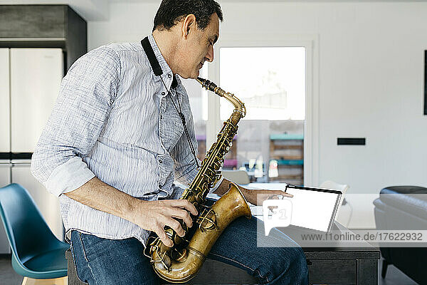 Musician with saxophone using tablet PC sitting on table at home+