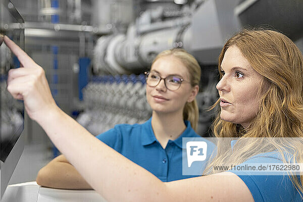 Technician explaining using touch screen device to trainee in factory