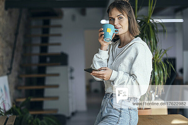 Woman with mobile phone having tea at home