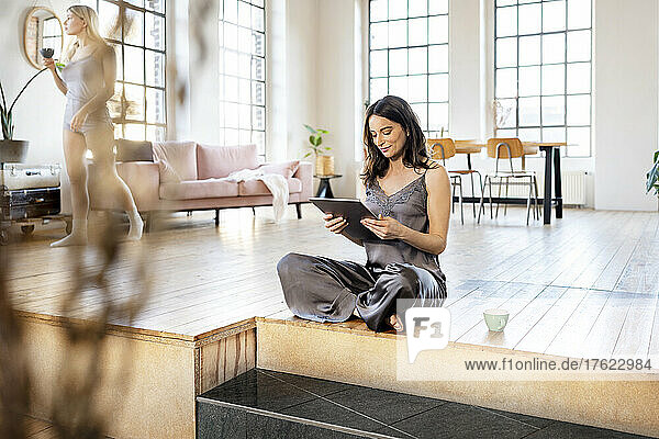 Geschäftsfrau mit Tablet-PC sitzt zu Hause auf der Diele im Wohnzimmer