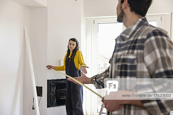 Confused woman with measuring tape talking with boyfriend in new living room