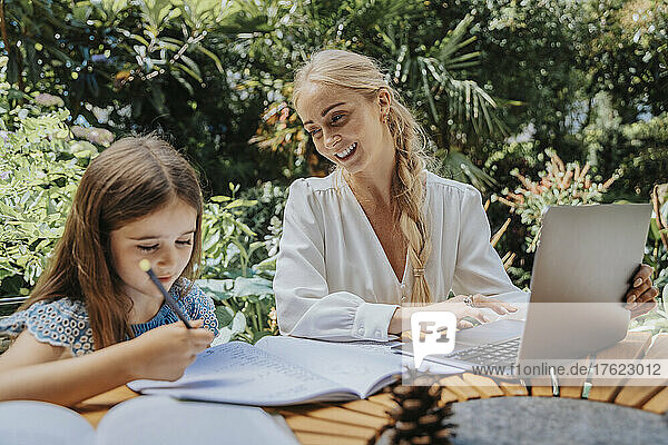 Smiling mother looking at daughter studying in yard