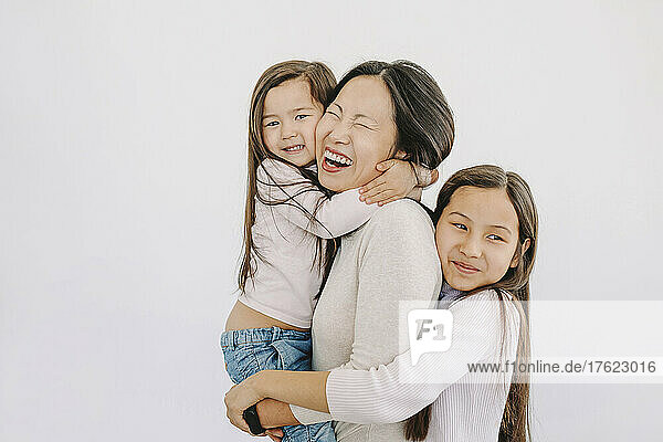Cute daughters embracing happy mother by white background