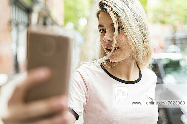 Teenager with blond hair taking selfie through mobile phone