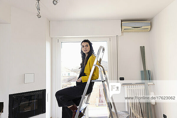 Nachdenkliche Frau sitzt auf Leiter im neuen Wohnzimmer
