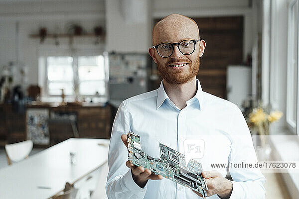 Smiling young businessman standing with circuit board in office