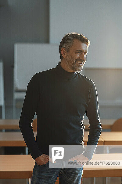 Happy businessman with hands in pockets at office