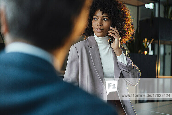 Businesswoman talking on smart phone by colleague in office