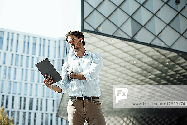 Businessman using tablet PC outside office building on sunny day