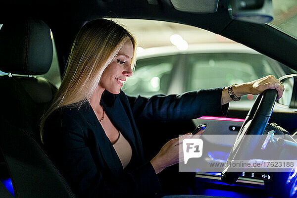 Lächelnde blonde Frau benutzt Smartphone im Auto