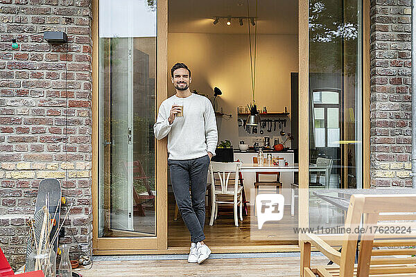 Smiling man with glass of coffee leaning on doorway