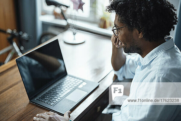 Happy man wearing eyeglasses sitting with laptop at table