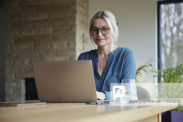 Blonde Frau sitzt am Tisch und benutzt Laptop