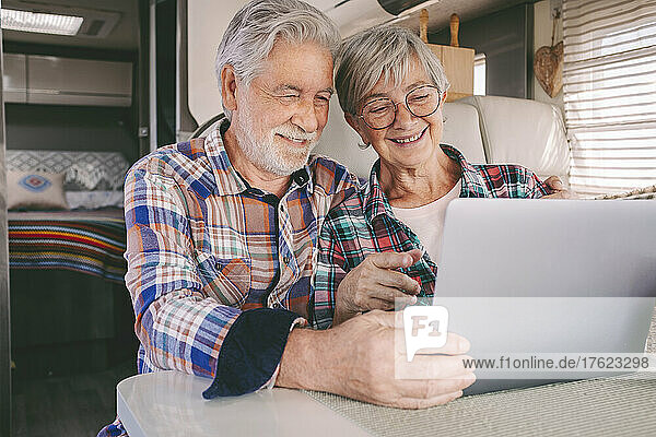 Happy senior couple using laptop in camper van