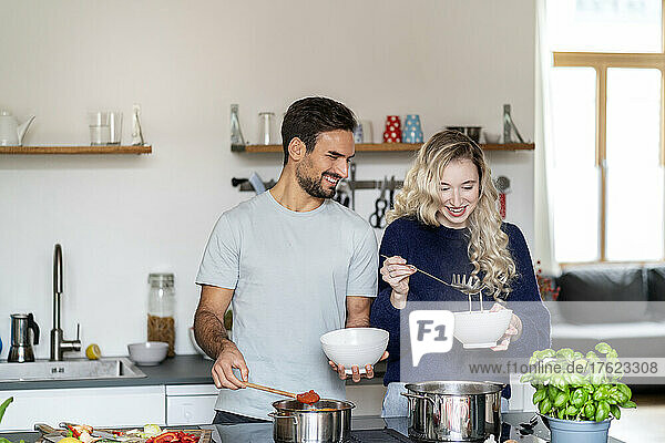 Happy couple serving food in bowls standing at kitchen island