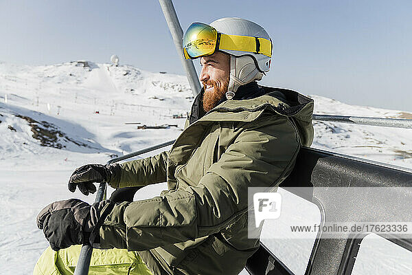 Young man wearing ski helmet and goggles sitting on lift