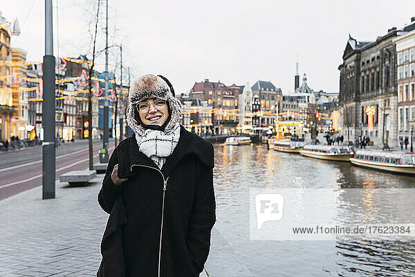 Smiling woman in winter hat by canal in city