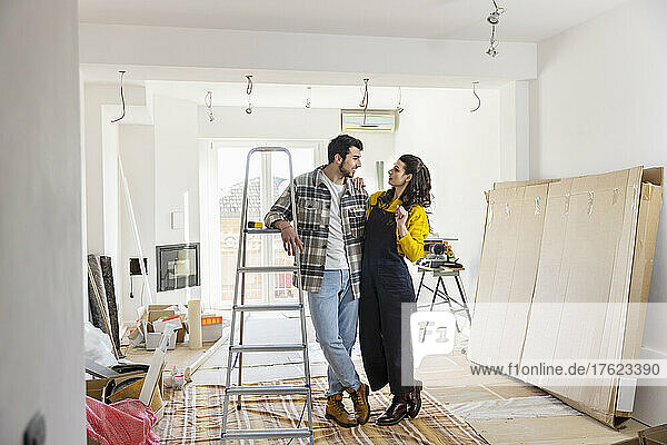 Young couple renovating home standing by ladder in living room