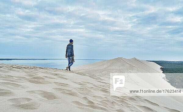 Woman walking on sand dune under cloudy sky