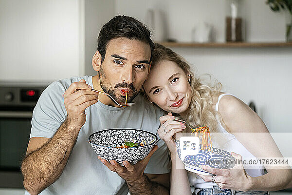 Smiling man and woman eating spaghetti at home