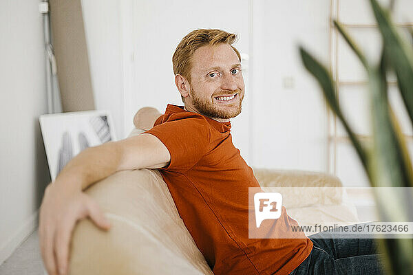 Happy young man sitting on sofa in living room at home