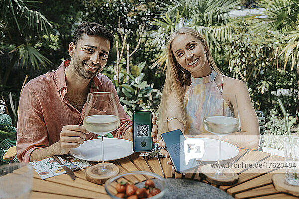 Smiling couple showing QR codes on smart phones at restaurant