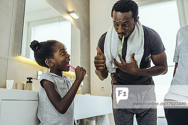 Vater zeigt Tochter beim Zähneputzen im Badezimmer die Daumen