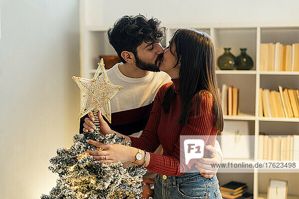 Affectionate couple kissing each other in front of Christmas tree at home