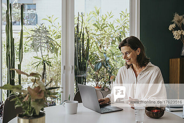 Smiling freelancer working with laptop on desk at home office