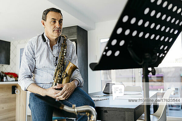 Musician sitting with saxophone looking at music stand in kitchen