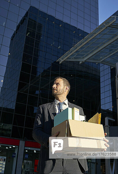 Businessman with office belongings standing in front of office building
