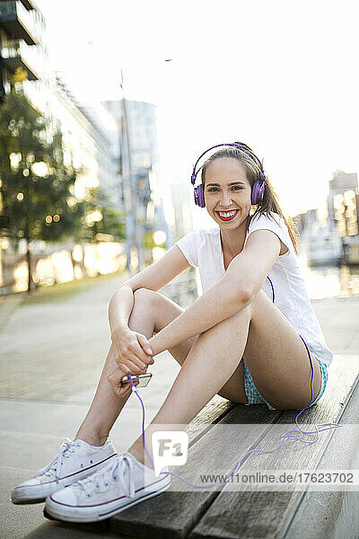 Happy woman listening music through headphones on bench