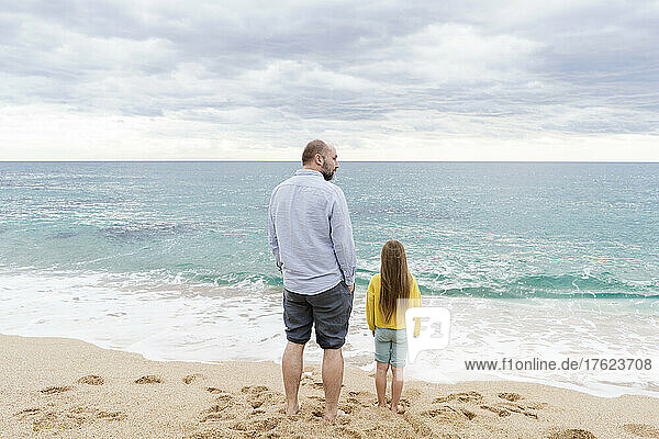Waves splashing towards father and daughter standing at beach