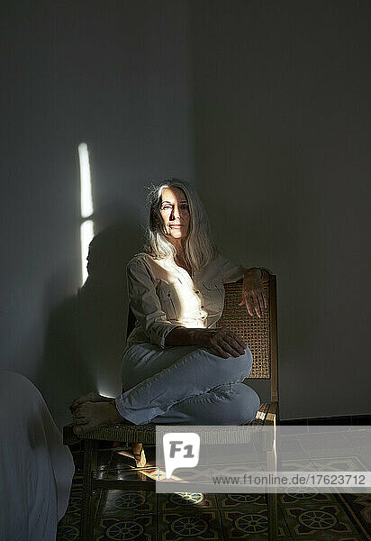 Woman sitting on chair with sunlight over her at home