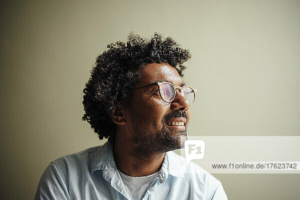 Smiling man with curly hair wearing eyeglasses at wall