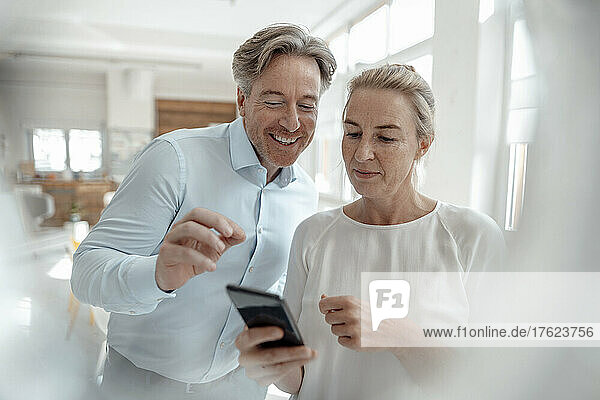 Businesswoman sharing smart phone with smiling businessman in office