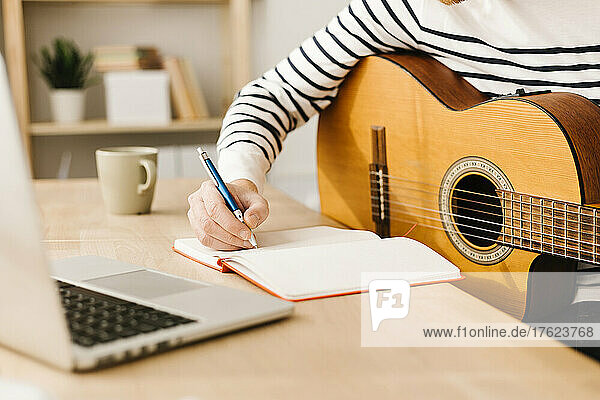Mann mit Gitarre schreibt Musiknote am Tisch