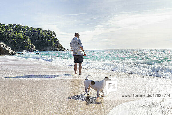 Mann steht neben Hund am Strand
