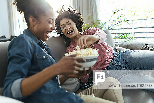Cheerful friends enjoying popcorn sitting on sofa at home