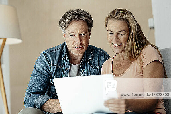Smiling woman holding laptop sitting with man at home