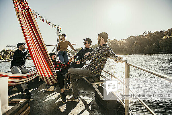 Happy friends spending leisure time together sitting on boat on sunny day