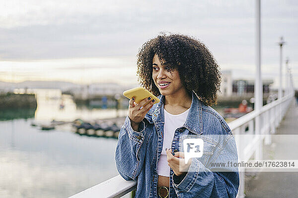 Afro woman talking on speaker smart phone at waterfront