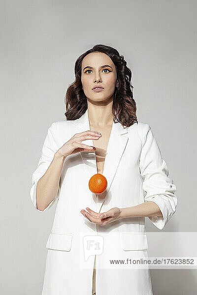 Young woman playing with tangerine standing against white background