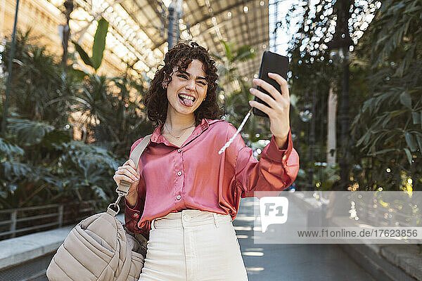 Woman sticking out tongue and taking selfie on smart phone