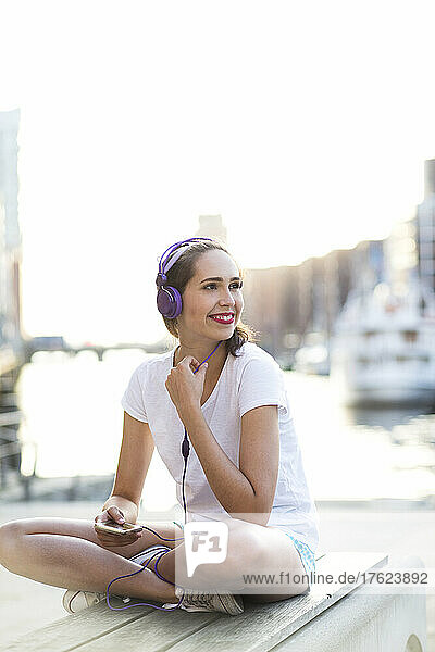 Glückliche Frau mit Kopfhörern sitzt auf Bank