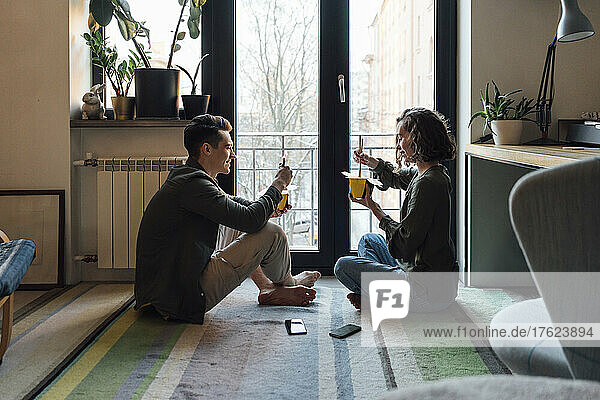 Junges Paar mit Essen zum Mitnehmen sitzt zu Hause am Fenster