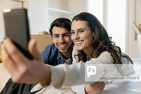 Lächelndes Paar macht Selfie mit Smartphone im Schlafzimmer seines neuen Zuhauses