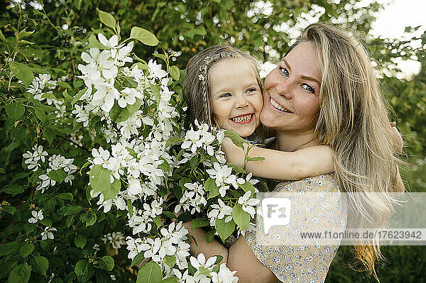 Happy mother with cute daughter standing by flowering bush